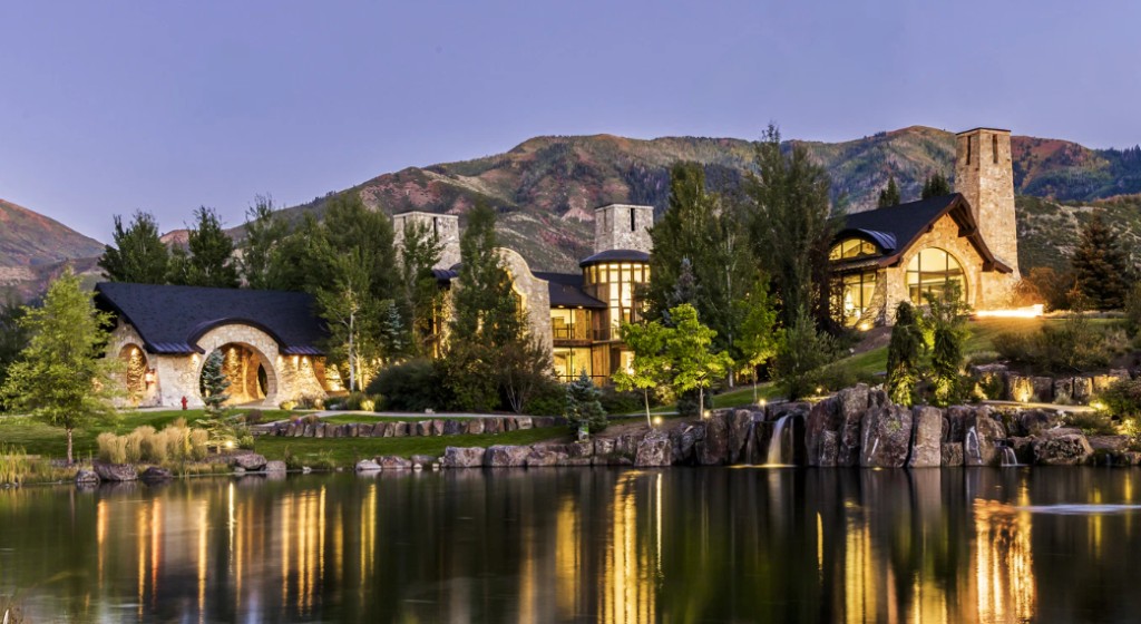 Luxury mountain estate at dusk with warm interior light and reflecting pond