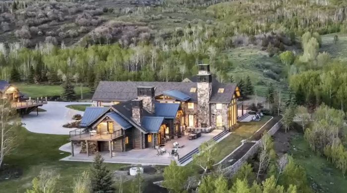 Aerial of a luxury mountain lodge at dusk with warm interior light and patio